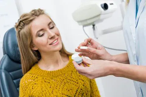 Young woman in a yellow sweater smiling during a contact lens fitting