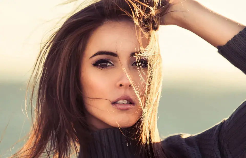 Woman with long brown hair lifting it from her forehead in golden evening light