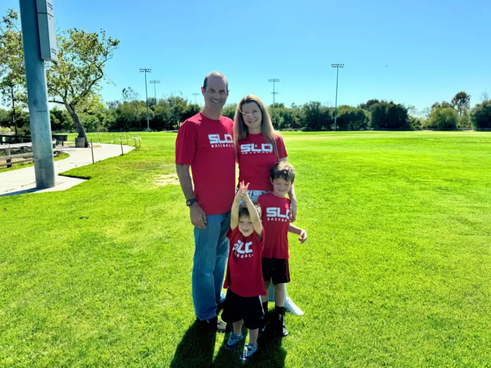 Dr. Justin Hellman and Dr. Gina Hellman with their two sons on a sunny lawn, all in red SLO shirts